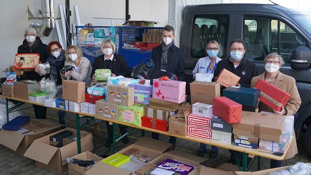 Sieben Personen mit Schutzmasken stehen hinter einem Tisch voller Spendenkartons im Freien, bereit für die Verteilung.